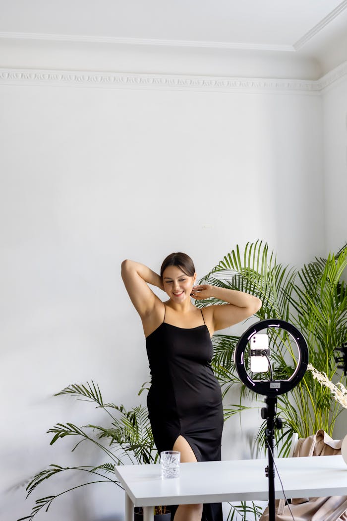 home-hero-1 Young woman posing joyfully indoors with a camera setup, embodying modern lifestyle.
